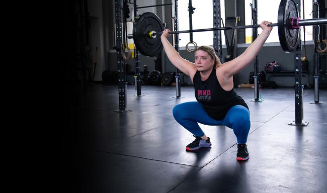 Ashley Farley crouches while holding a weighted barbell in a gym.