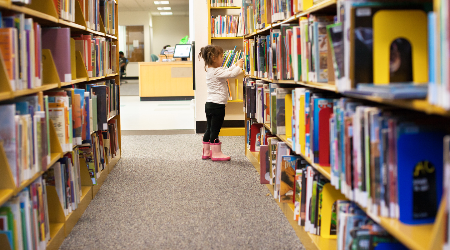 A young girl looks at shelves of books at a library