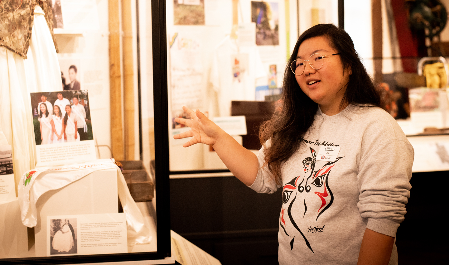 Lillian Xie gestures toward objects in the Bainbridge Island Historical Museum.