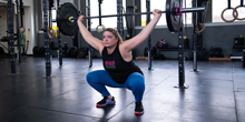 Ashley Farley crouches while holding a weighted barbell in a gym.