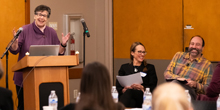 UW President Ana Mari Cauce speaks at a lectern while Monika Sengul-Jones and Ryan Calo laugh.