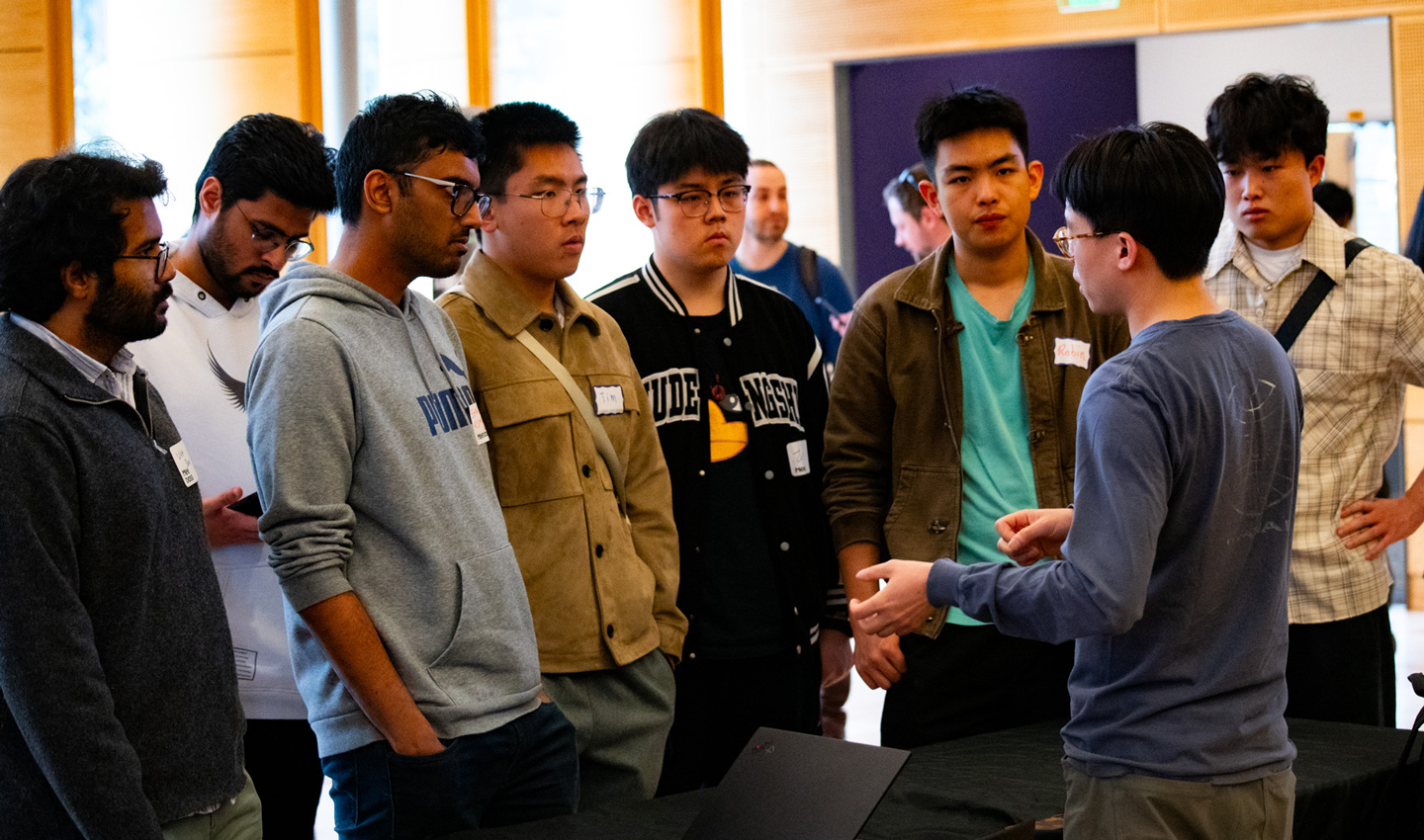 Several young men gather around a company's representative at a table.