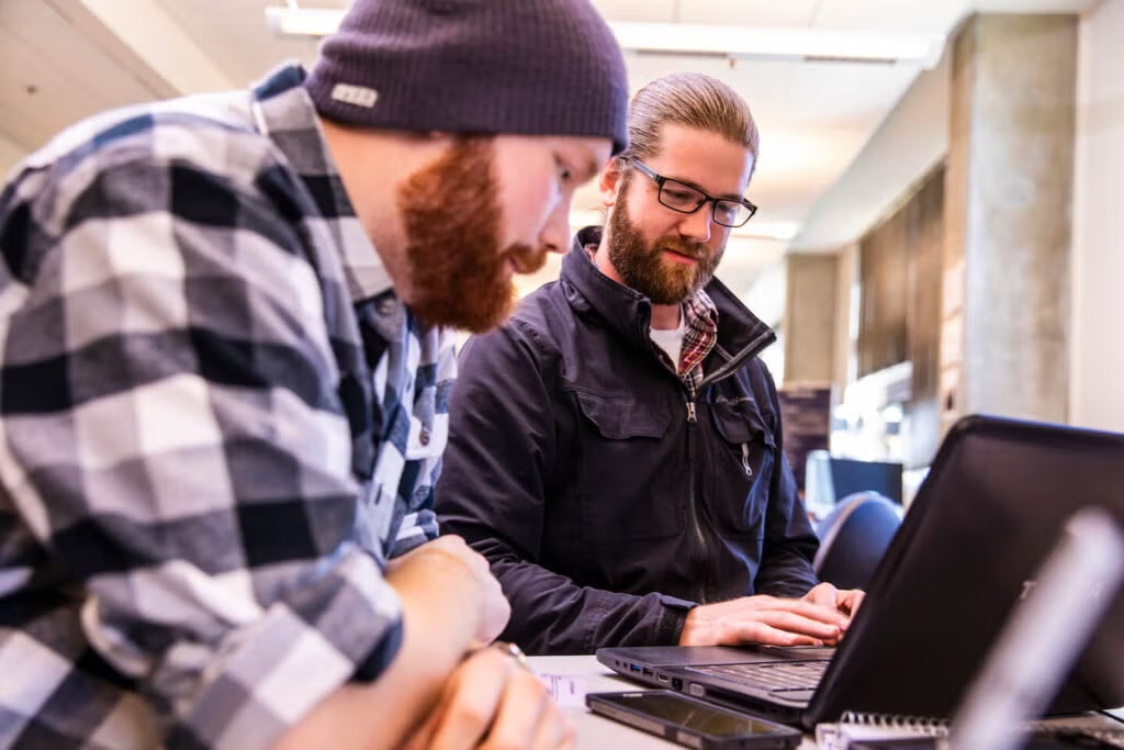 Two men work at a laptop computer.