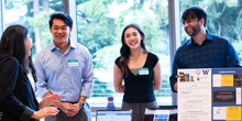 A group of project presenters speak to a visitor.