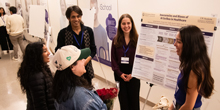 Five people gather and speak around a display.