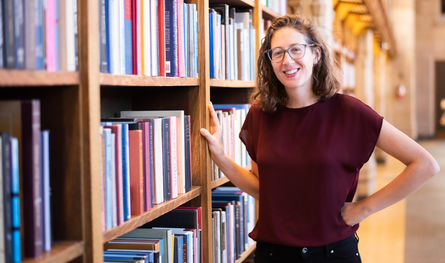 Melanie Walsh stands next to bookshelves in a library.