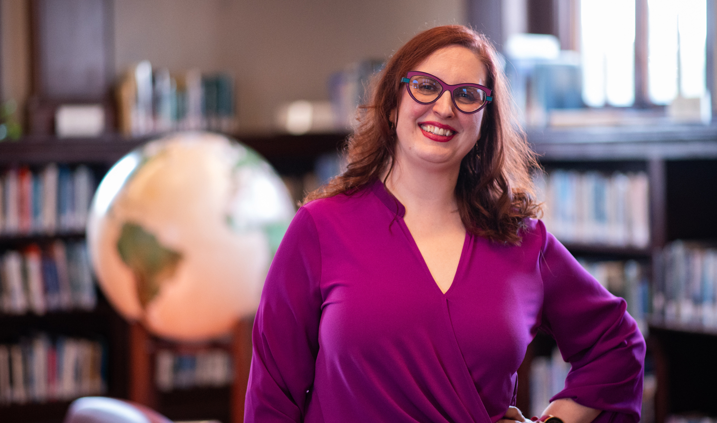 Melody Sky Weaver stands with a globe and bookshelves in the background.