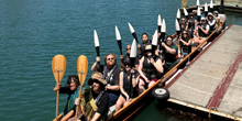 Students hold paddles up while seated in a canoe.