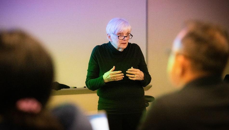 Annie Searle lectures, viewed from behind students seated in a classroom.