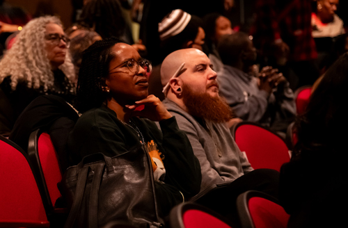 A woman and a man listen while seated in an auditorium.