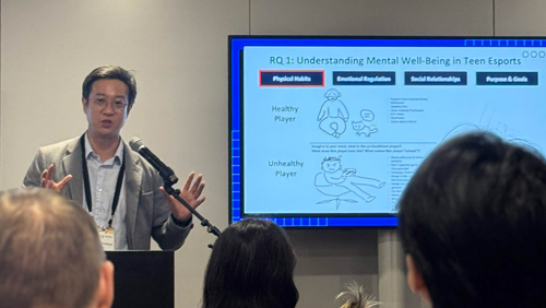 Johnny Cho presents to a group of listeners in front of a video screen.