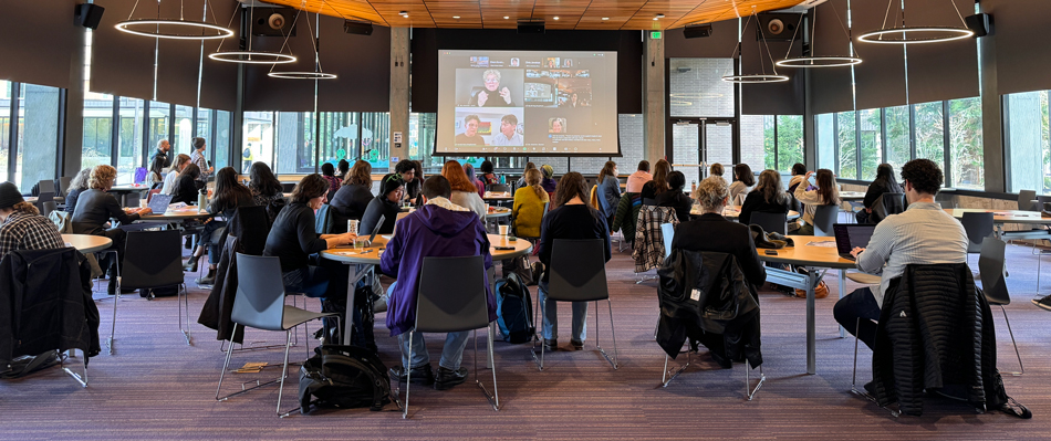 People seated around tables while a presentation occurs onscreen in front of them.