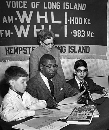Spencer Shaw at a microphone with children at WHL radio in Long Island, New York.