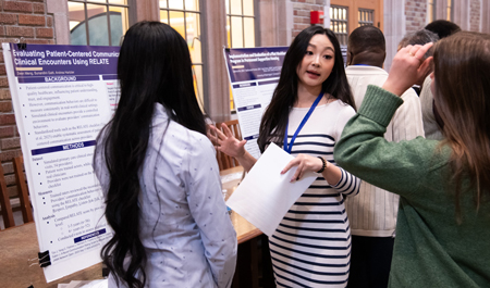 A young woman speaks to visitors in front of a research poster.
