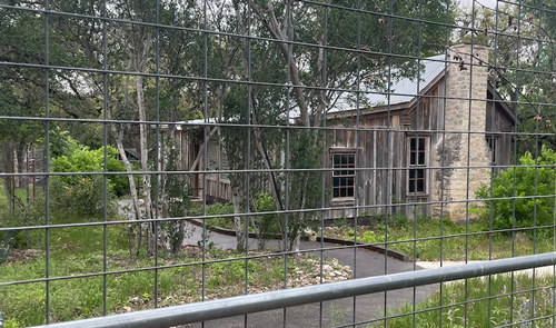 Image of an aged log house behind a fence.