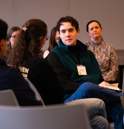 A man speaks with a woman while surrounded by other discussion participants.