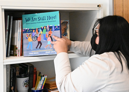 Bishop thumbs through her collection of children’s books by Native authors in her office. Along with her job in health sciences, she has worked with the American Indian Library Association to advocate for Native authors.