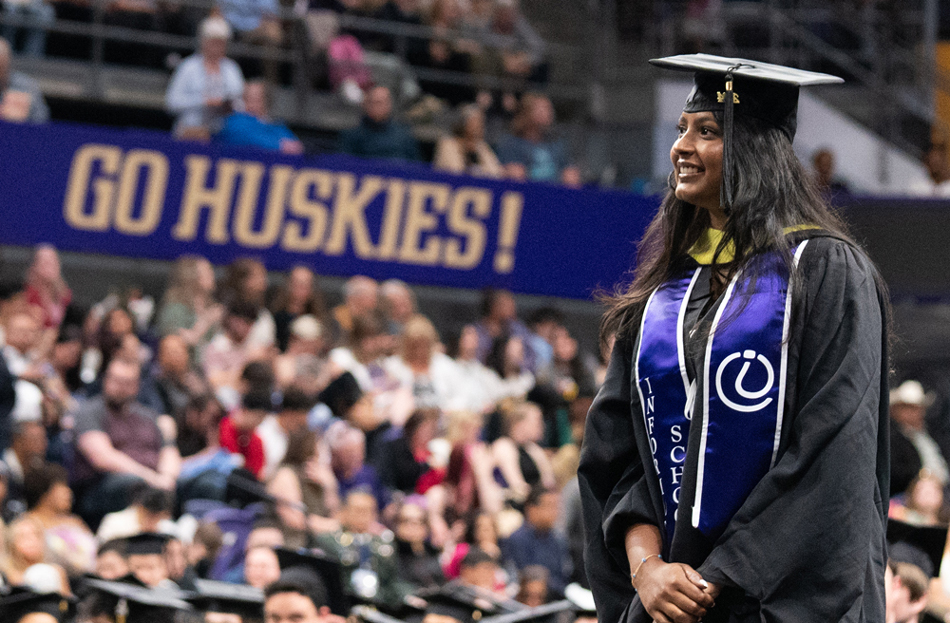 A woman walks toward the stage with a "go Huskies" banner in the background