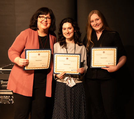Three women hold their award certificates.