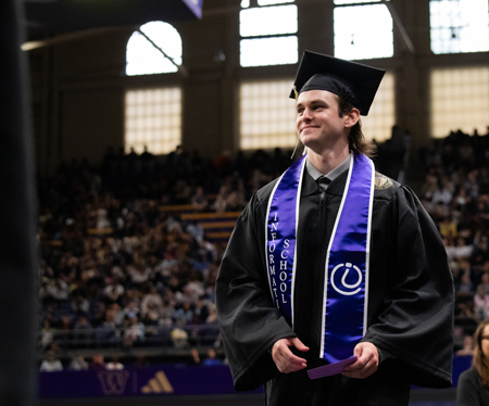 A man in graduation clothing smiles as he walks..