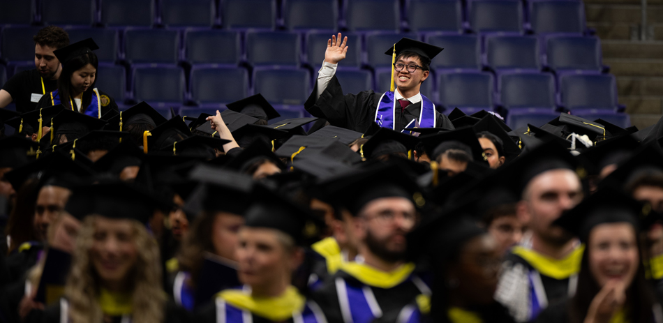 A man stands among other graduates and smiles.