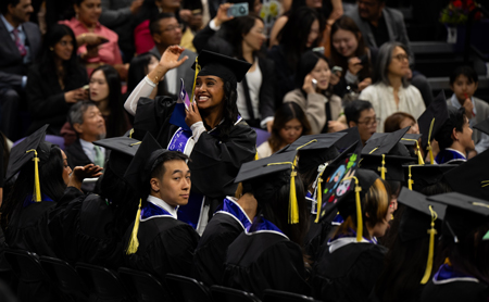 A woman stands among other graduates and smiles.