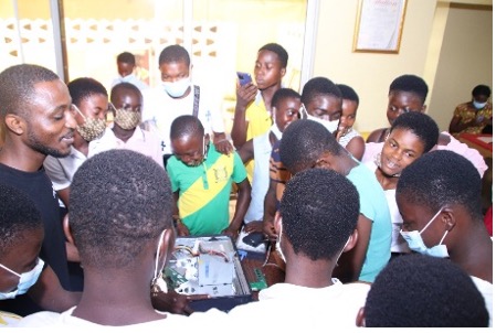 A crowd of about 20 youths gather around a computer.