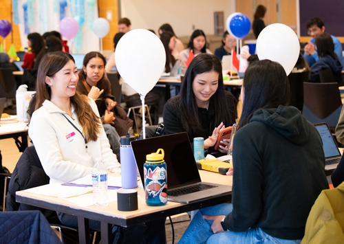 A woman laughs as another looks at her phone while seated.