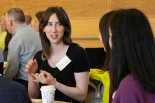 A woman speaks with others while seated at an event.