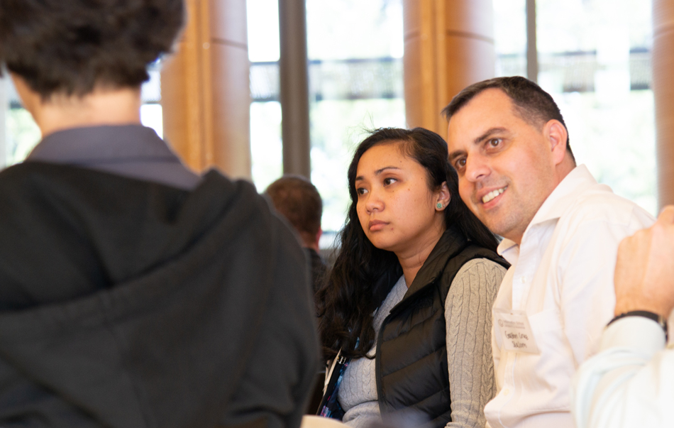 A man and woman listen while seated at a table during an event.