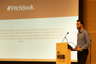 A man speaks at a lectern in front of a screen featuring PitchBook.