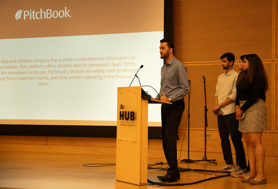 Four students on stage with a slide behind them regarding PitchBook.