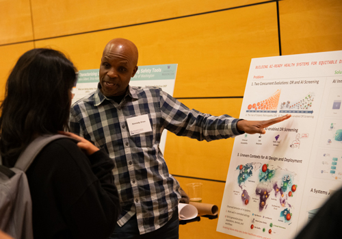 Kennedy Orwa gestures toward a poster while speaking to a person with their back to the camera.