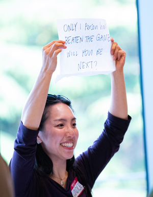A woman holds up a sign reading "Only 1 person has beaten the game. Will you be next?"