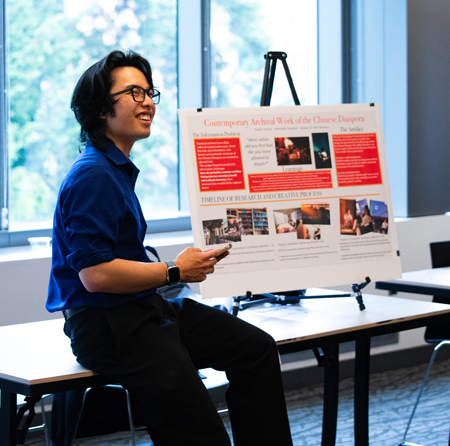 A man smiles as he shows his project poster.