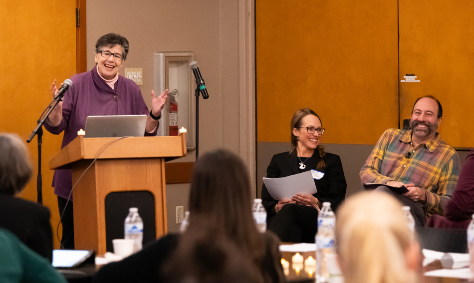 UW President Ana Mari Cauce speaks at a lectern while Monika Sengul-Jones and Ryan Calo laugh.